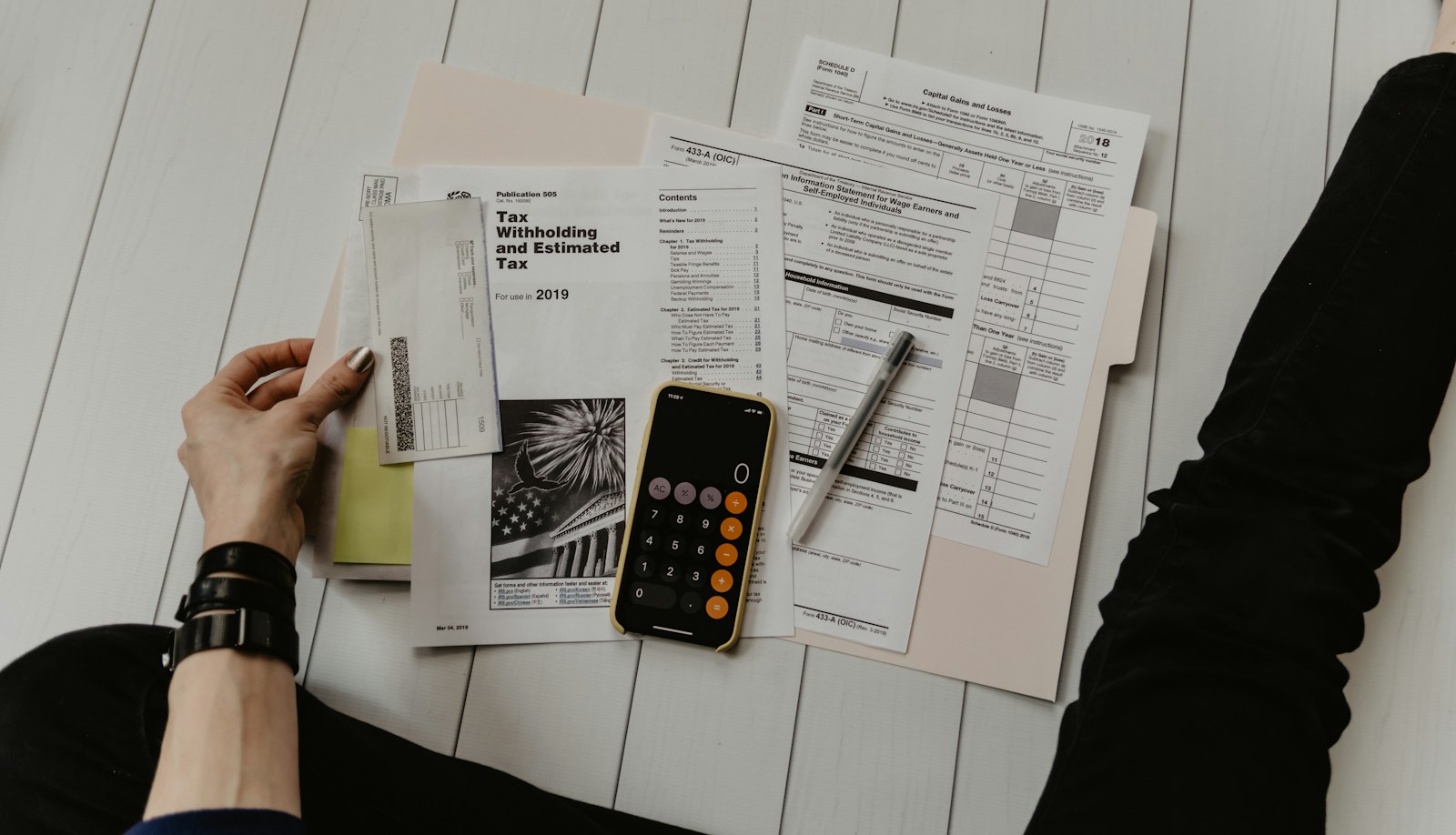 Forms, receipts and a calculator phone spread across a folder on a desk